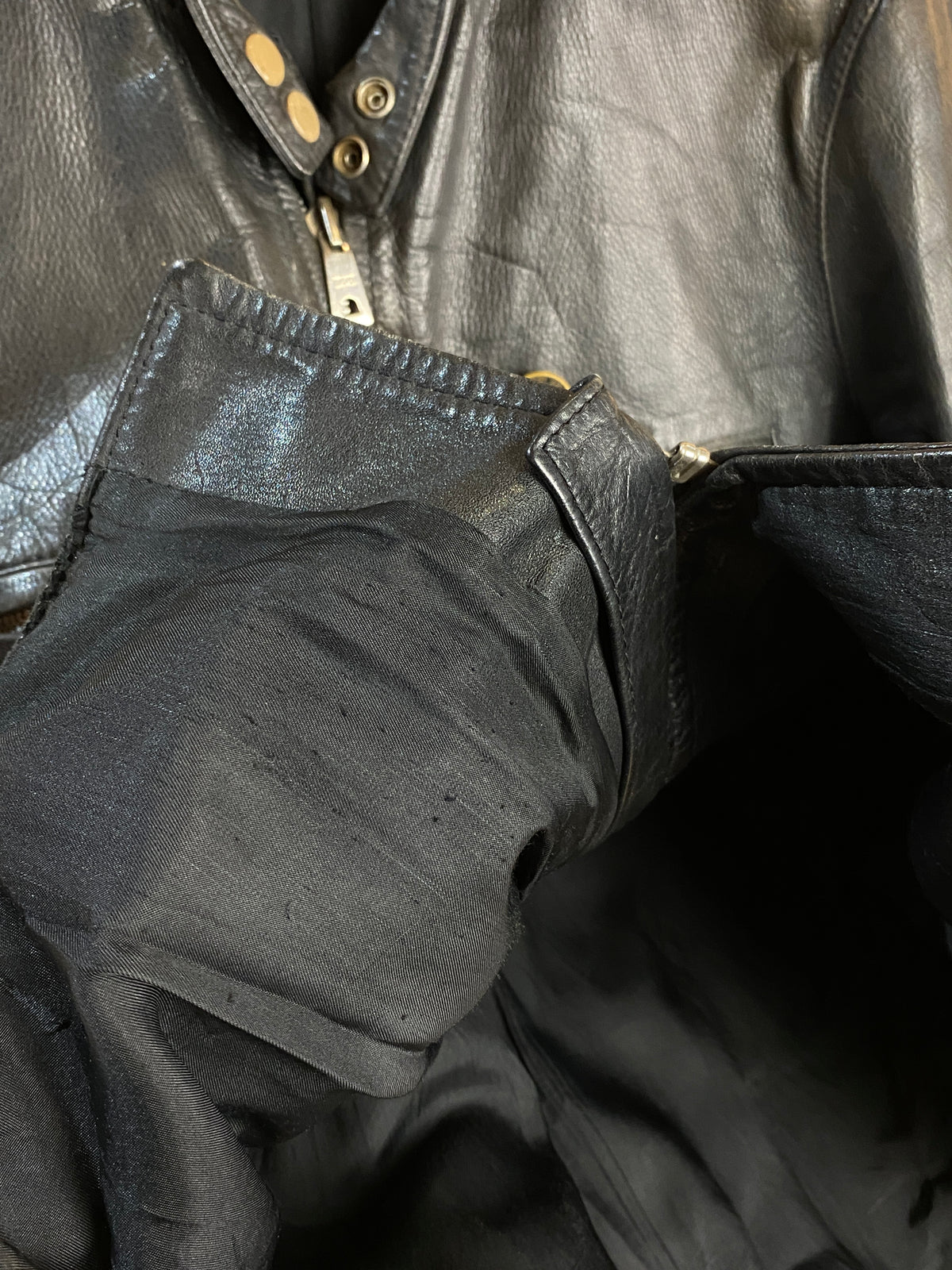 Close-up of the inside of the 1940s Black Leather Cafe Racer Jacket - S by Arkive Vintage, highlighting the shiny inner lining, a stitched seam, and part of a zippered pocket—a detail characteristic of authentic vintage cafe racer jackets.